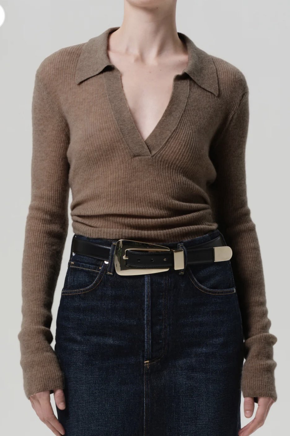 Brown ribbed sweater and dark jeans with a belt on a plain background