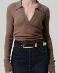 Brown ribbed sweater and dark jeans with a belt on a plain background